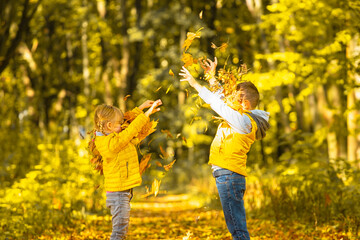 Two smiling kids throwing autumn leaves in the park