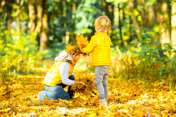 Happy children playing with falling leaves in autumn park