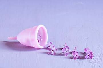 Obraz na płótnie Canvas Woman health concept. Pink menstrual cup with lilac flower on violet background.