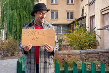 Cheerful man holding a sign with the text forgive me on the city street to ask for forgiveness