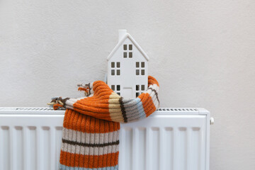 Figure of house and warm clothes on heating radiator. Home heating expenses and savings concept. 
