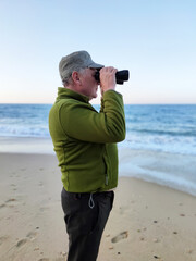 an adult man looks at the sea horizon with binoculars