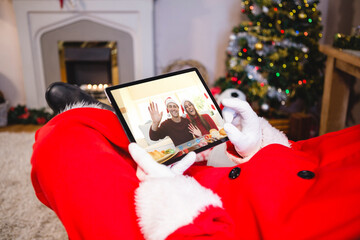 Santa claus making laptop christmas video call with waving caucasian couple