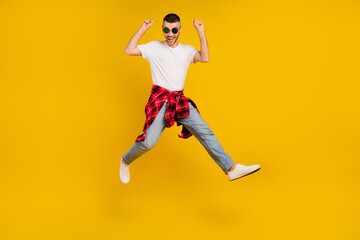Fototapeta na wymiar Full body photo of young funky man jump up winner enjoy wear plaid shirt tied on waist isolated on yellow color background