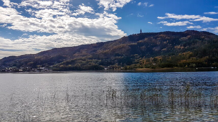 A view through the dried grass on a lake and a hill in the back. There is a tower on top of a hill. Clear and sunny day. Slopes of the hills are turning golden. Calm surface of the lake.