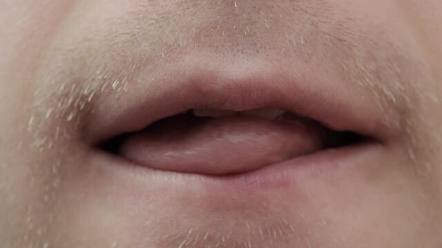 Unshaven man licks lips with tongue, macro. Emotions