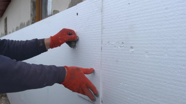 Construction worker installing styrofoam insulation sheets on house facade wall for thermal protection