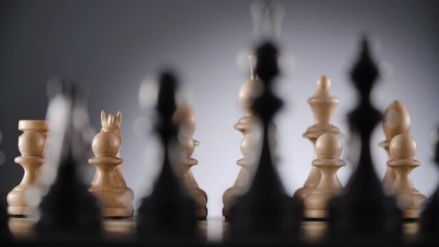 Close-up of chessboard with lines of white and black wooden chess figures ready to play with blurred foreground and background