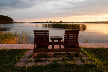 Fototapeta na wymiar Two wooden chairs on the bank of the Ob River in Siberia at sunset