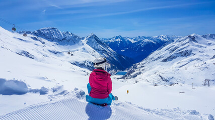Snowboarding girl sitting on the snow in Moelltaler Gletscher, Austria, enjoying the view. Lots of snow in the mountains. Endless Alps chain. Winter wonderland, paradise. Calmness and happiness.