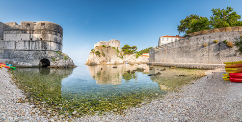 Obraz premium View of small water bay near old city of Dubrovnik. Ancient fort Lovrijenac near small harbor with boats. Sunny day.