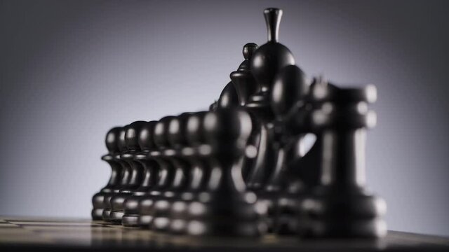 Close-up of rotating chessboard with lines of black wooden chess figures ready to play with blurred foreground and background