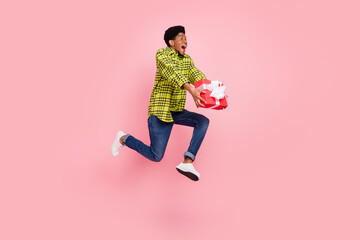 Full length photo of millennial sweet brunette guy jump hold present wear shirt jeans sneakers isolated on pink background