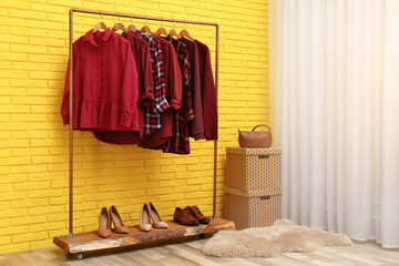 Rack with stylish clothes near yellow brick wall indoors