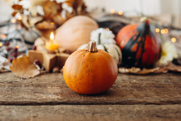 Ripe pumpkins near a burning candle and autumn leaves against a cozy blanket and rustic wooden...