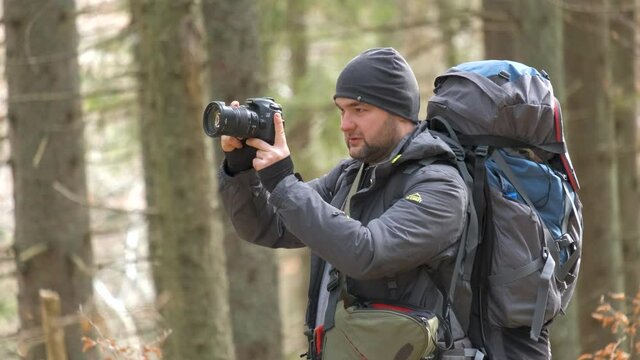 Photographer with hiking backpack taking pictures of nature with digital photo camera