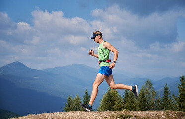 Guy jumping while running by mountain trails. Summer trail running marathon in mountains on...