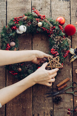 Woman making Christmas wreath, Fir handmade Chirstmas wreath with wooden star and red berries, rustic advent decoration, Christmas wreath making workshop