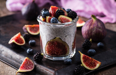 Healthy chia pudding with figs and dark berries in glass on the rustic background. Selective focus....