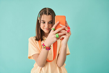 Girl making selfie while using smartphone standing isolated on turquoise studio background