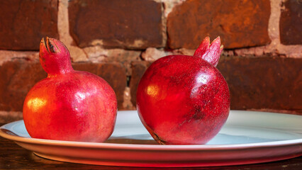 Two fruit juicy Spanish pomegranate on porcelain plate on a red brick wall background.