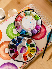 Watercolour wheel of colours and a black paint brush with painted doughnuts in the background