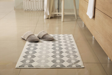 Soft bath mat and slippers on floor indoors - obrazy, fototapety, plakaty