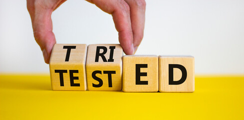 Tried and tested symbol. Businessman turns wooden cubes and changes the concept word 'tried' to 'tested' on a beautiful white background. Copy space. Business and tried and tested concept.