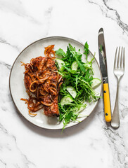 Delicious comfort food -  barbecue pork chop  with caramelized onion and arugula cucumber salad on a light background, top view