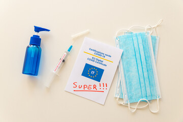 Covid Green Pass with text "super", blue mask, hand sanitizer, and syringe labeled "vaccine booster dose" on a white surface. Introduction of the super green pass and third dose of the vaccine, or boo