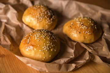 Fresh homemade burger buns with sesame seeds, on the table in craft baking paper. cooking blog, recipes, menu. selective focus. appetizing background