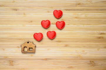 Red little hearts over a wooden figurine of a toy house on a wooden background.