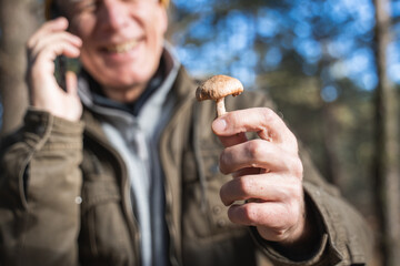 Senior man holding mushroom and chatting via smartphone with pleasure smile