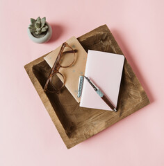 Carnets, stylo plume et lunettes dans un plateau en bois sur fond rose avec succulent - inspiration...