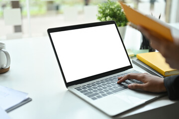Photo of hands typing on a white blank screen computer laptop at the modern working desk.