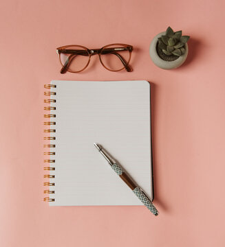 Carnet &agrave; spirale avec page blanche, stylo plume, lunettes et succulent sur fond rose pour l'inspiration d'&eacute;crire - travailler au f&eacute;minin