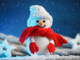 Knitted toy snowman in a hat, mittens and scarf. Blue background with falling snow