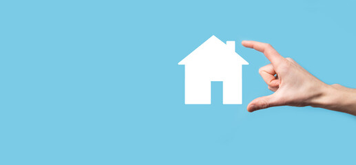 Fototapeta na wymiar Male hand holding house icon on blue background. Property insurance and security concept.Real estate concept.Banner with copy space.