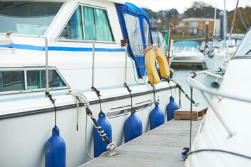 White boat white blue fenders suspended between a boat and dockside for protection. Maritime fenders