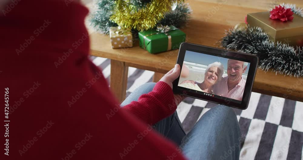 Sticker Caucasian man waving and using tablet for christmas video call with smiling couple on screen