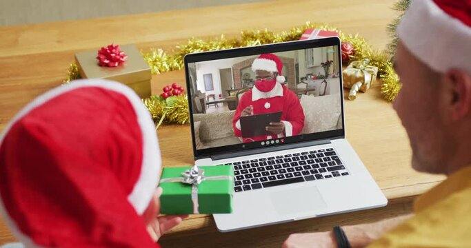 Caucasian father and son with santa hats using laptop for christmas video call with santa on screen
