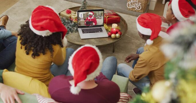 Diverse family with santa hats using laptop for christmas video call with santa on screen