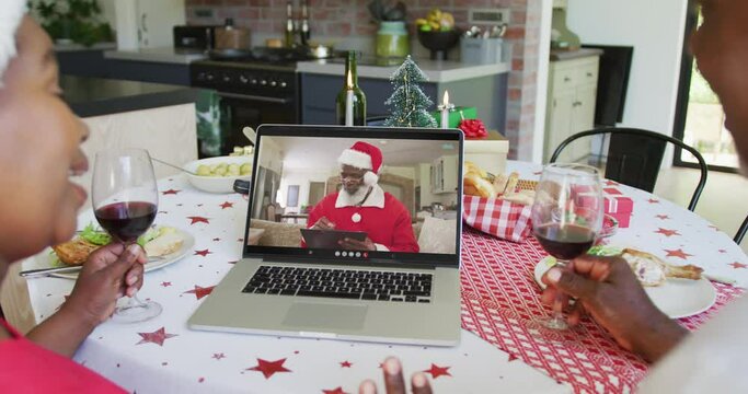 African american couple with wine using laptop for christmas video call with santa on screen