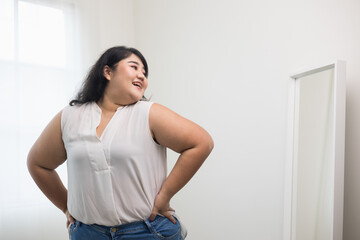 Fototapeta na wymiar Body positive plus size female clothing. Body positive plus size woman happily and is proud of herself looking at mirror at home. Try wearing clothes that measure the size.