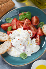Close-up of stracciatella di bufala with cherry tomatoes, green basil and ciabatta served on a turquoise plate, vertical shot