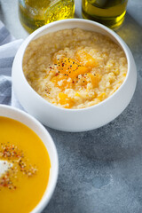 Millet porridge with addition of pumpkin served in a white bowl, vertical shot on a light-blue stone surface, middle close-up