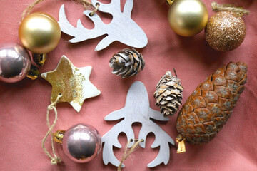 Wooden Christmas ornaments, gold and metallic baubles and pine cones on pink background. Flat lay.