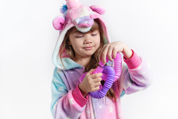 Cheerful little girl in unicorn pajamas plays in a popular toy poptube. An exciting children's game with multi-colored plastic pipes.