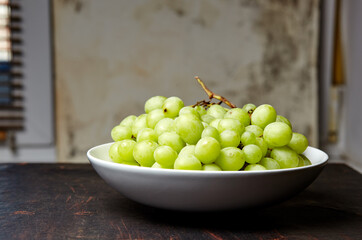 Branch of ripe green grape on plate. Juicy grapes on wooden background, closeup. Grapes on dark kitchen table with copy space