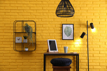 High wooden table with tablet and stool as stand up workplace near yellow brick wall. Stylish interior